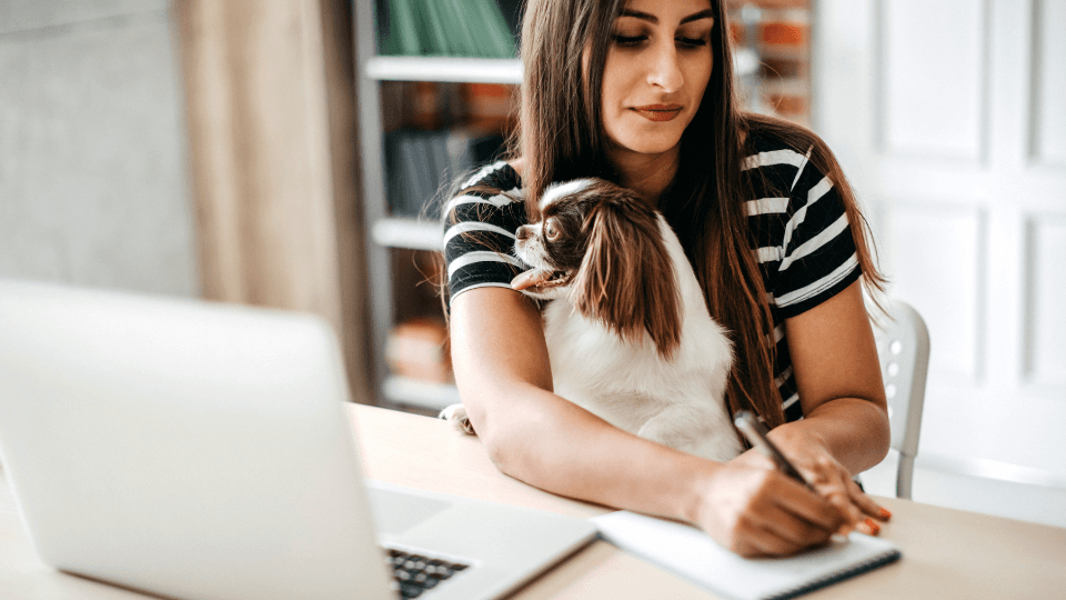 Woman sitting at desk signing paper with dog on lap